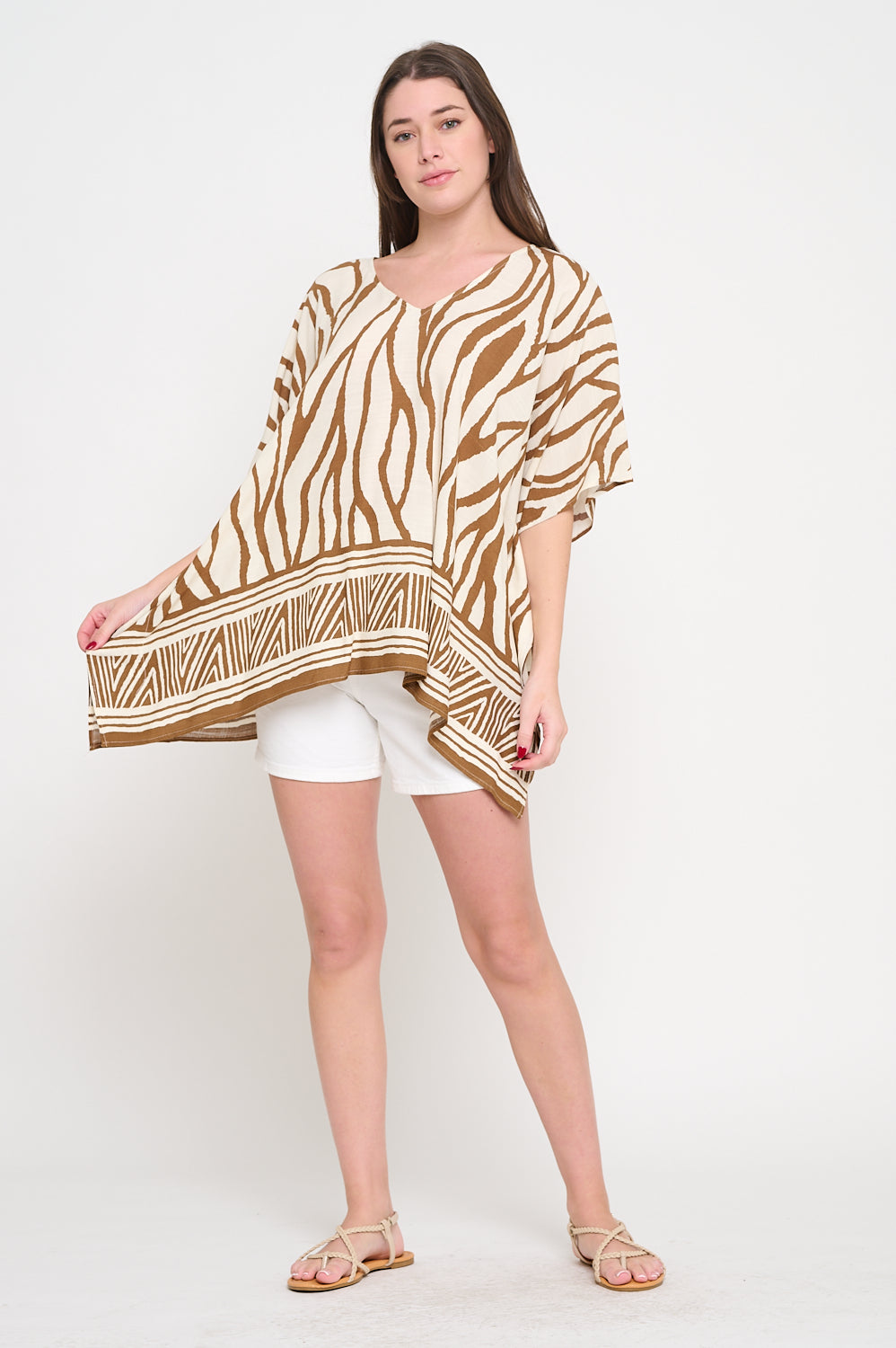 Woman wearing a V-neck tunic with zebra-inspired print in earthy tones and geometric border, styled with white shorts.