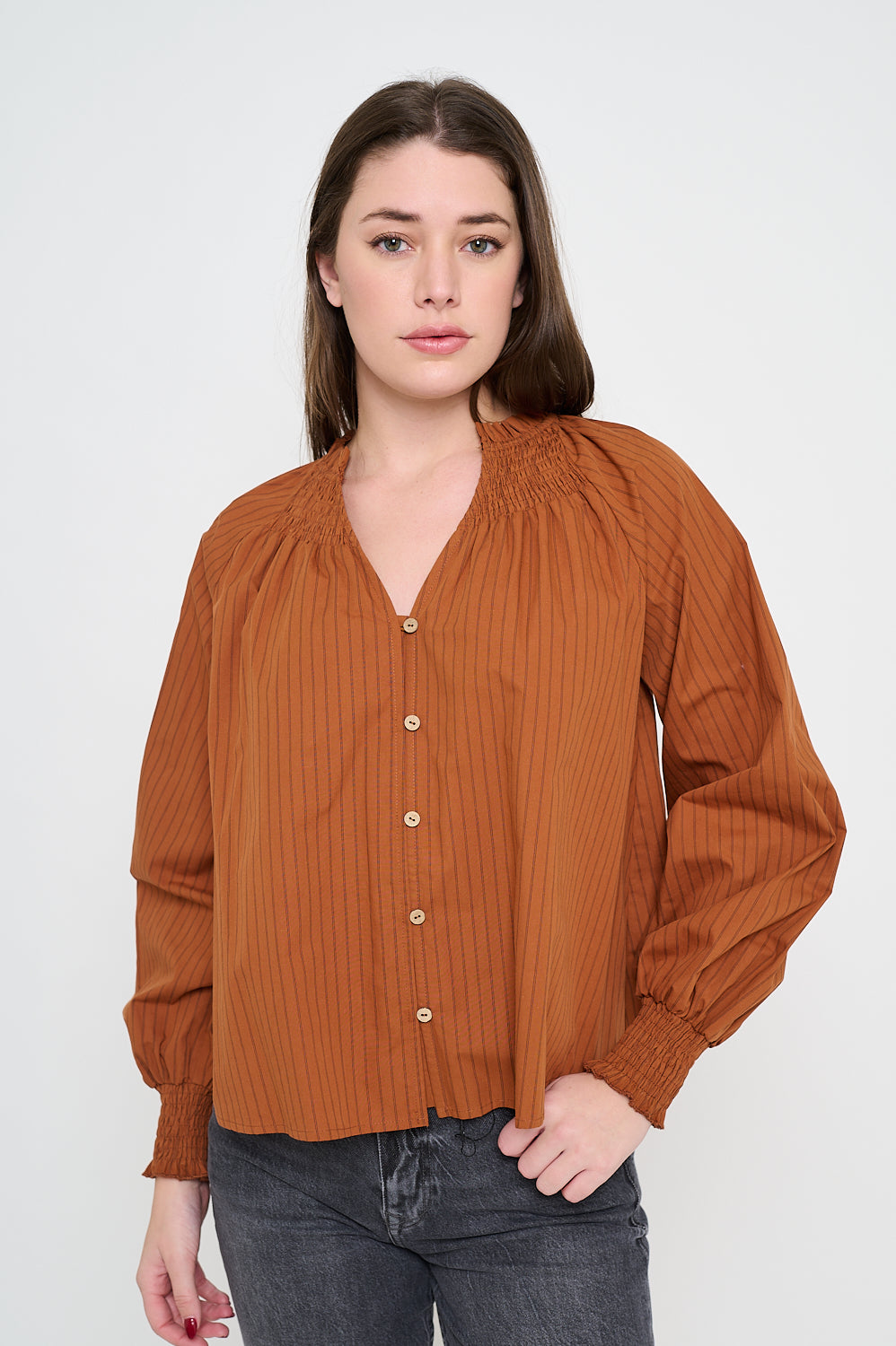 Woman wearing a long sleeve V-neck blouse in terracotta with tonal stripes, button front, and smocked cuffs.