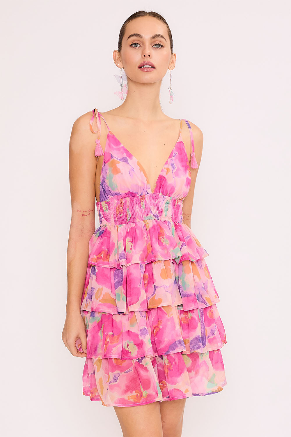 Model wearing a colorful tiered mini dress with a V-neckline, smocked waist, and watercolor floral print.