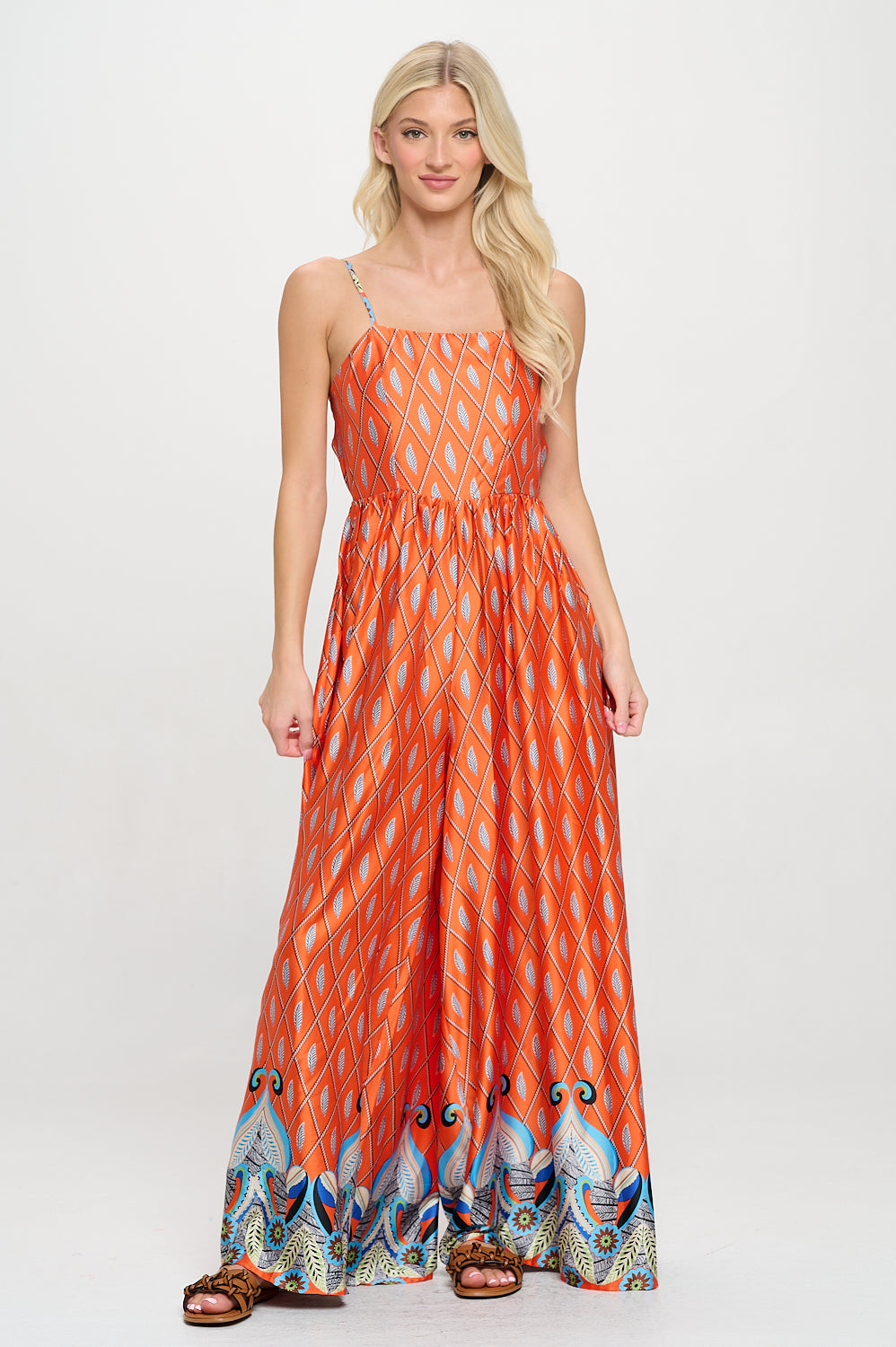 Model wearing a bold saffron printed wide-leg jumpsuit with square neckline and spaghetti straps—styled for vacation or resortwear moments.