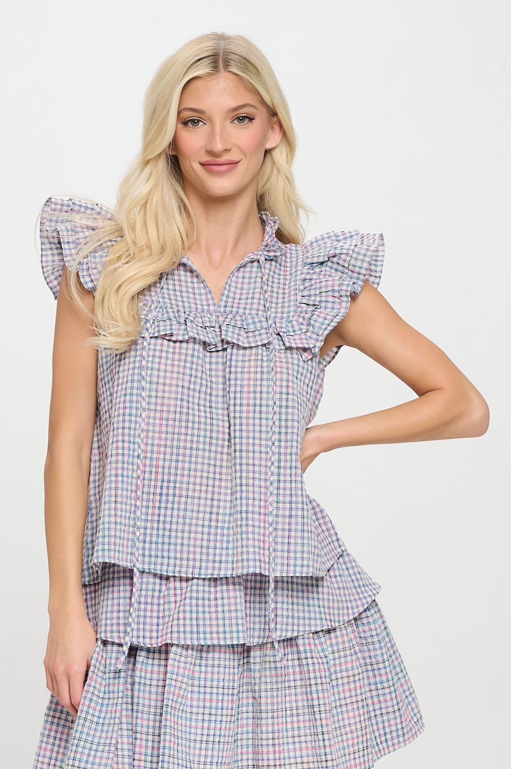 Model wearing a ruffled plaid top with flutter sleeves and v-neckline, styled in a relaxed fit for a breezy, summer-ready look.