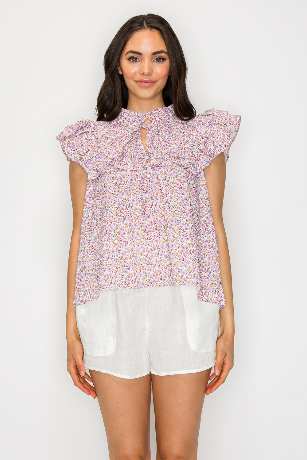 Model wearing a floral ruffle-sleeve blouse with keyhole neckline and breezy silhouette, paired with white summer shorts.