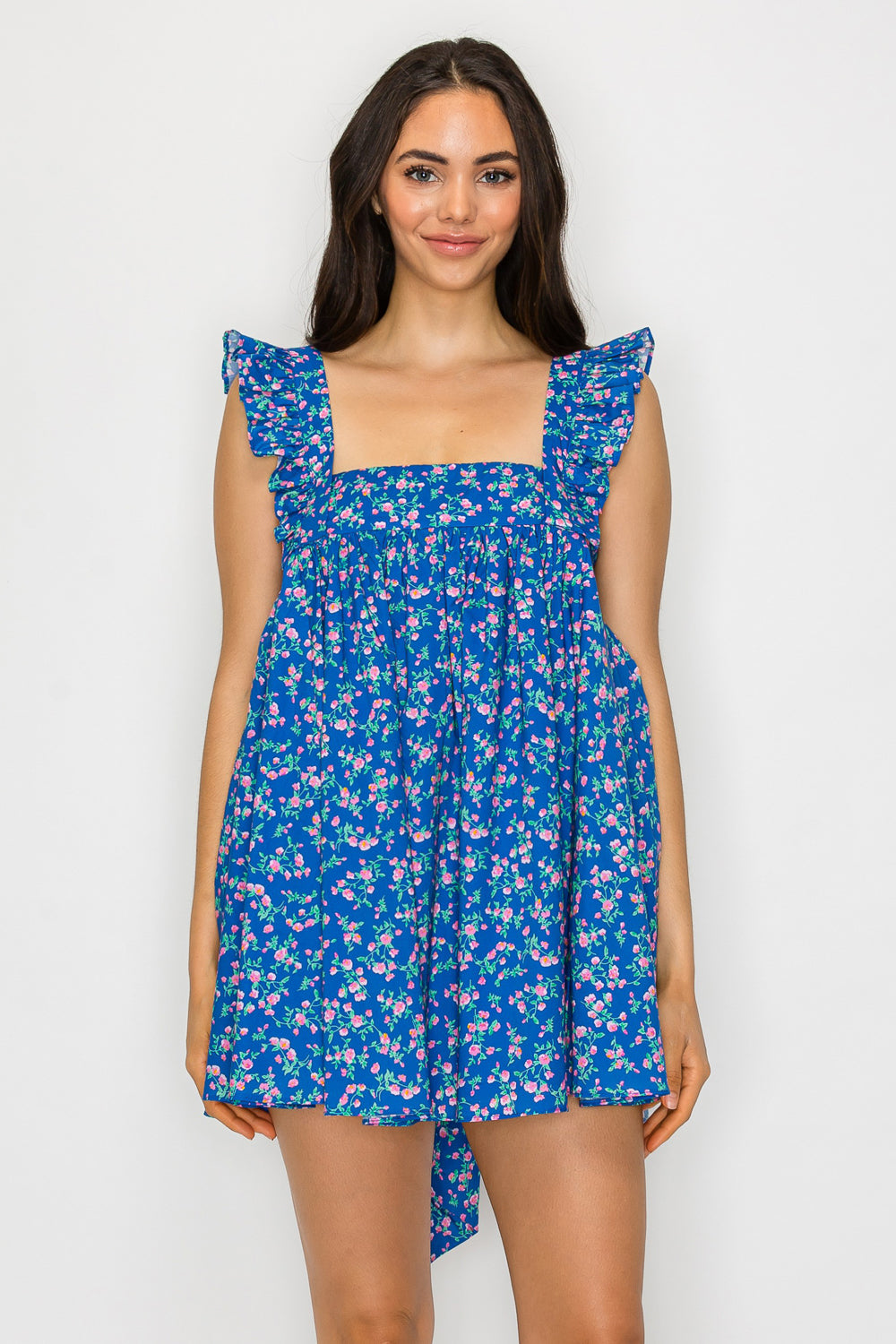 Model wearing a floral babydoll mini dress with ruffle straps, square neckline, and an oversized bow tie-back detail.