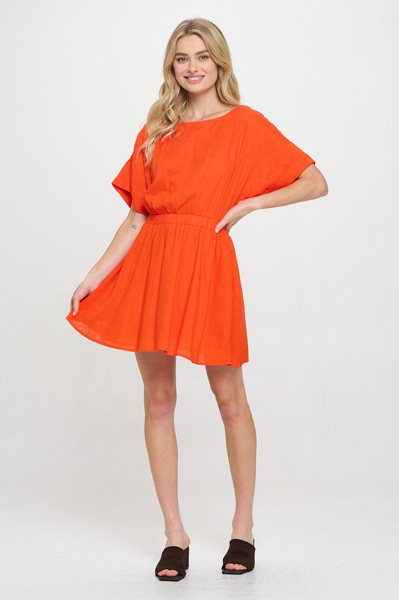 Model wearing an orange mini dress with elastic waist, short sleeves, and round neckline. Styled for summer vacations or casual outings.