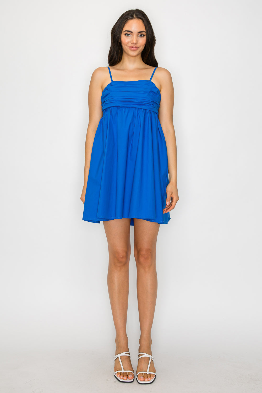 Model wearing a blue A-line short dress with ruched bodice, spaghetti straps, and oversized bow at the open back.