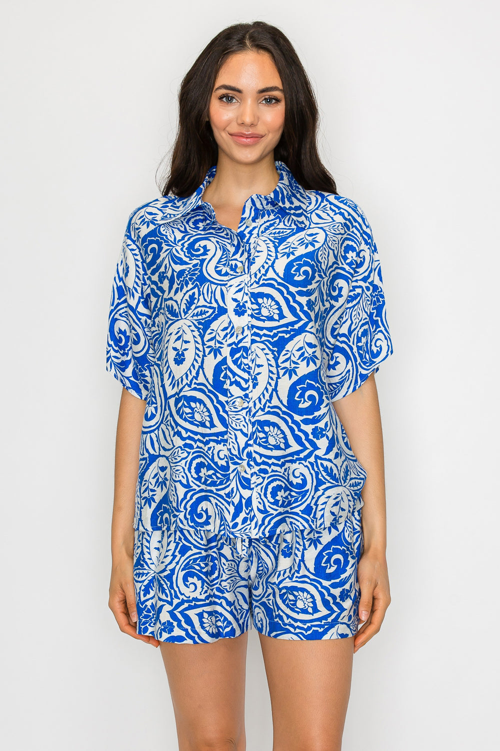 Model wearing a blue paisley short-sleeve button-down top and matching drawstring shorts in a relaxed resortwear set.