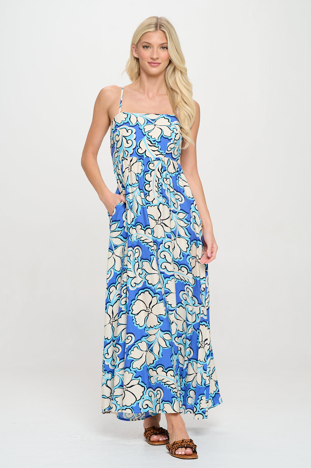 Model wearing a blue floral maxi dress with square neckline, spaghetti straps, and pockets—styled for resortwear or coastal vacation.
