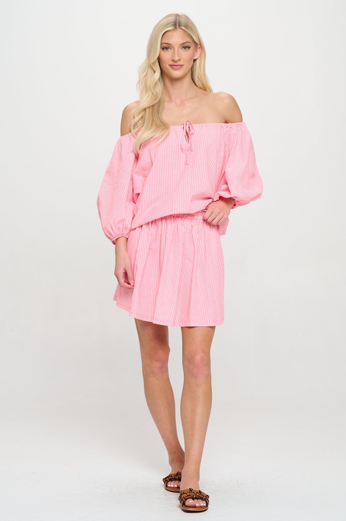 Model wearing an off-shoulder pink and white striped two-piece set with puff sleeves and matching mini skirt