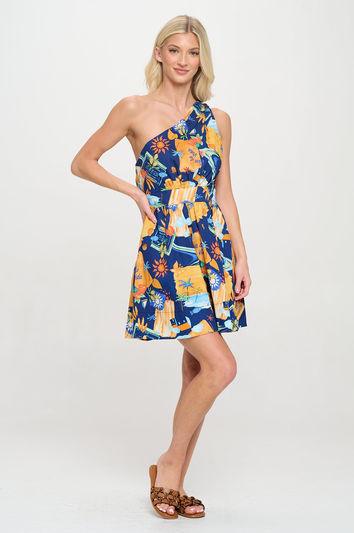 Model wearing Mediterranean Escape One Shoulder Dress with an asymmetric neckline, cinched waist, and flared skirt in a bold island print.