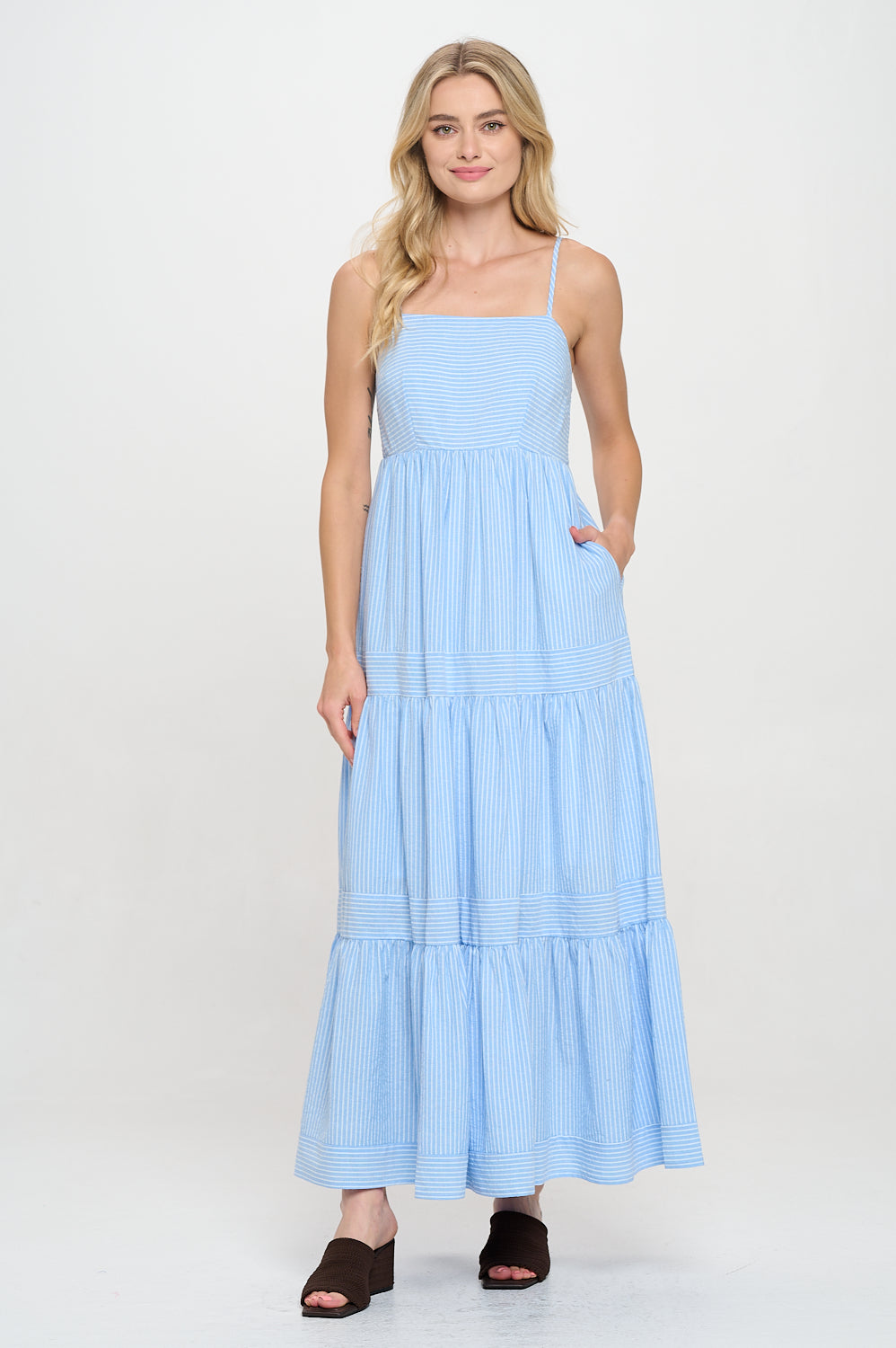 Model wearing a blue striped tiered maxi dress with spaghetti straps and pockets, styled for coastal travel or summer resortwear.