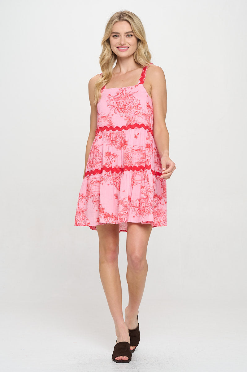 Woman wearing a pink ric-rac detailed mini dress with a square neckline, toile print, and tiered skirt.