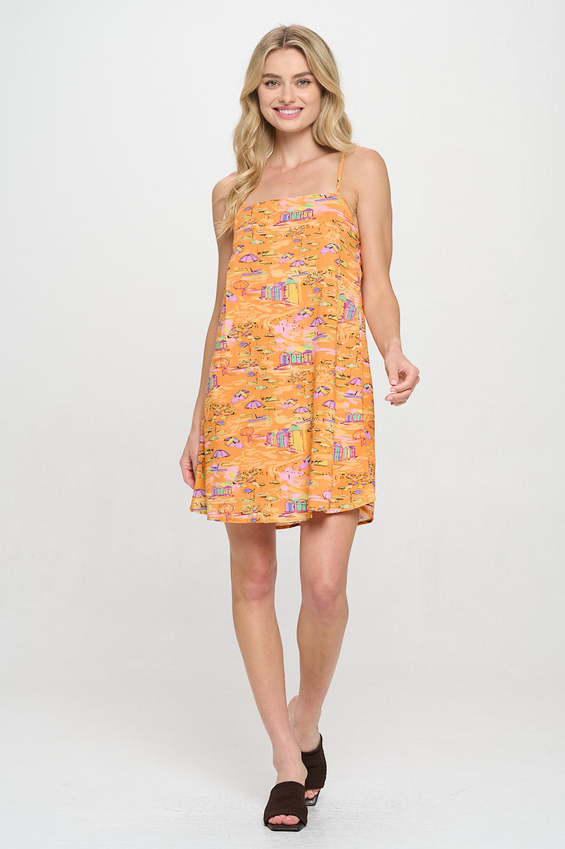 Model wearing a printed cami mini dress with adjustable spaghetti straps and square neckline. Styled for warm-weather vacations and resort days.