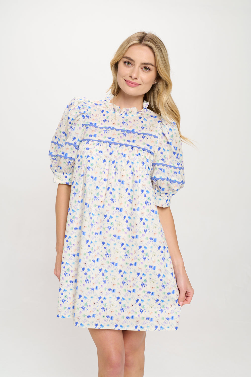 Model wearing a floral pintuck mini dress with puff sleeves, ruffle neckline, and lace trim.