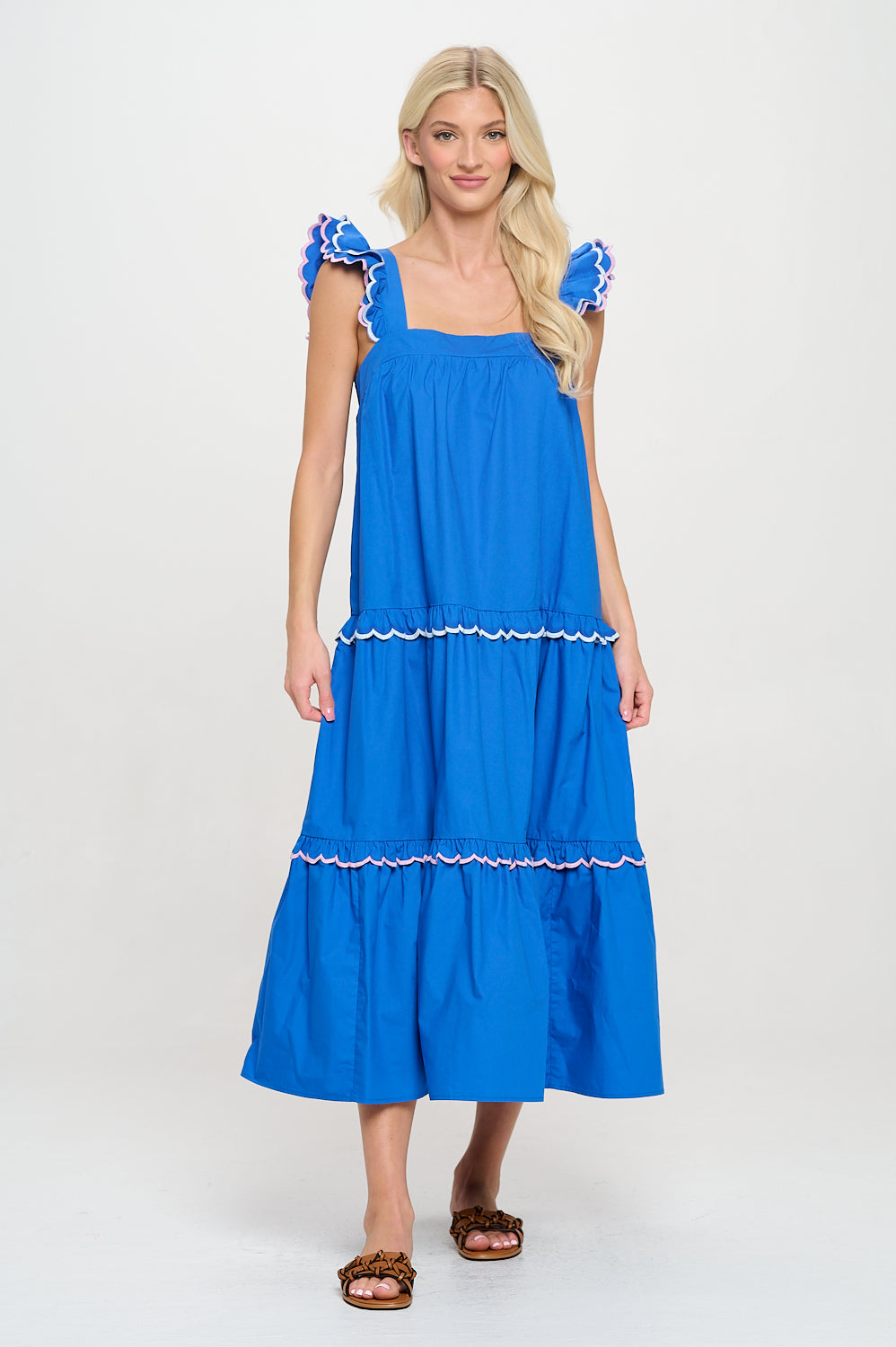Woman wearing a blue tiered maxi dress with scalloped flutter straps and square neckline – feminine resortwear for summer travel and coastal styling