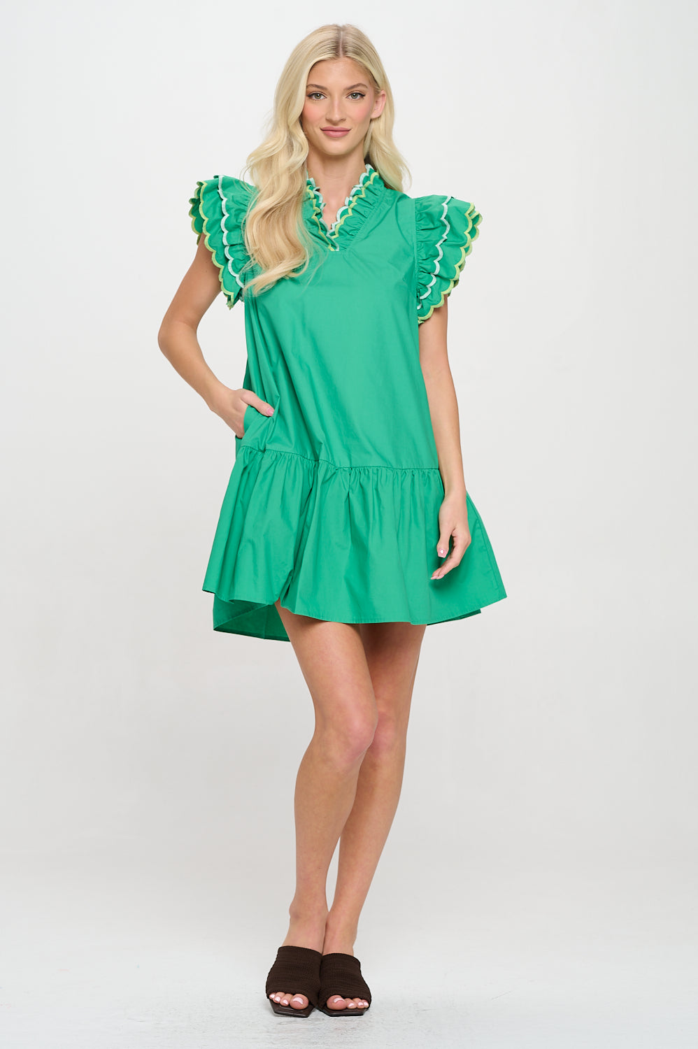 Model wearing a green mini dress with scalloped ruffle sleeves, split neckline, and pockets—styled for resort or vacation wear.