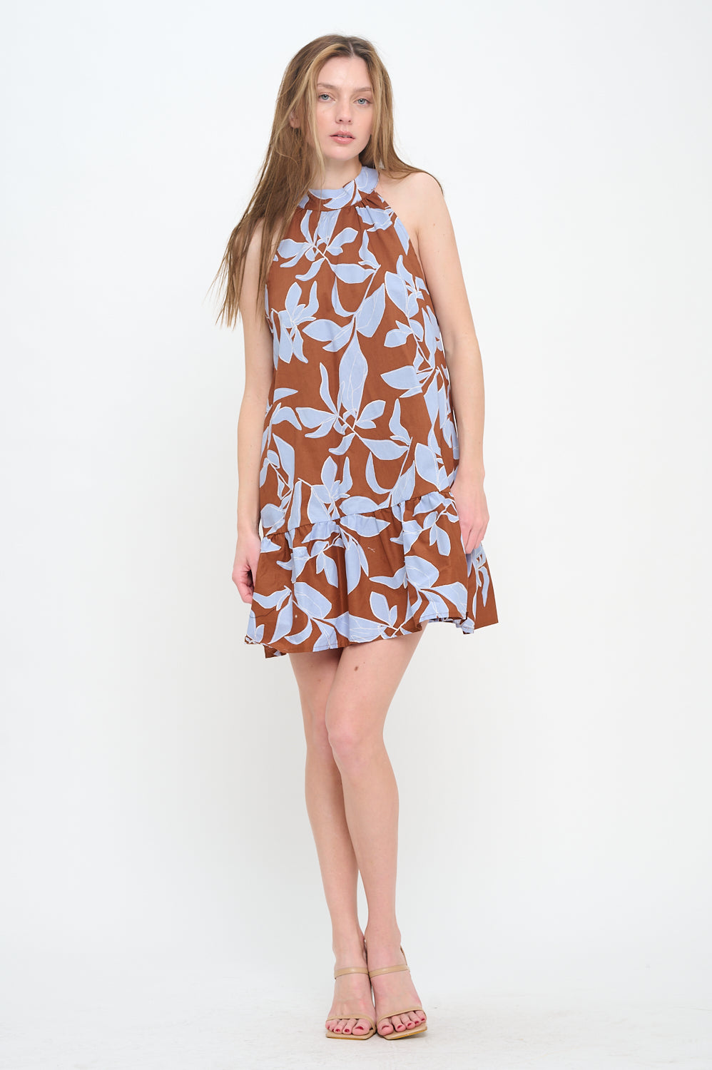 Woman wearing a sleeveless mini dress with a halter neckline and a brown-and-blue botanical print, featuring a relaxed fit and ruffled hem.