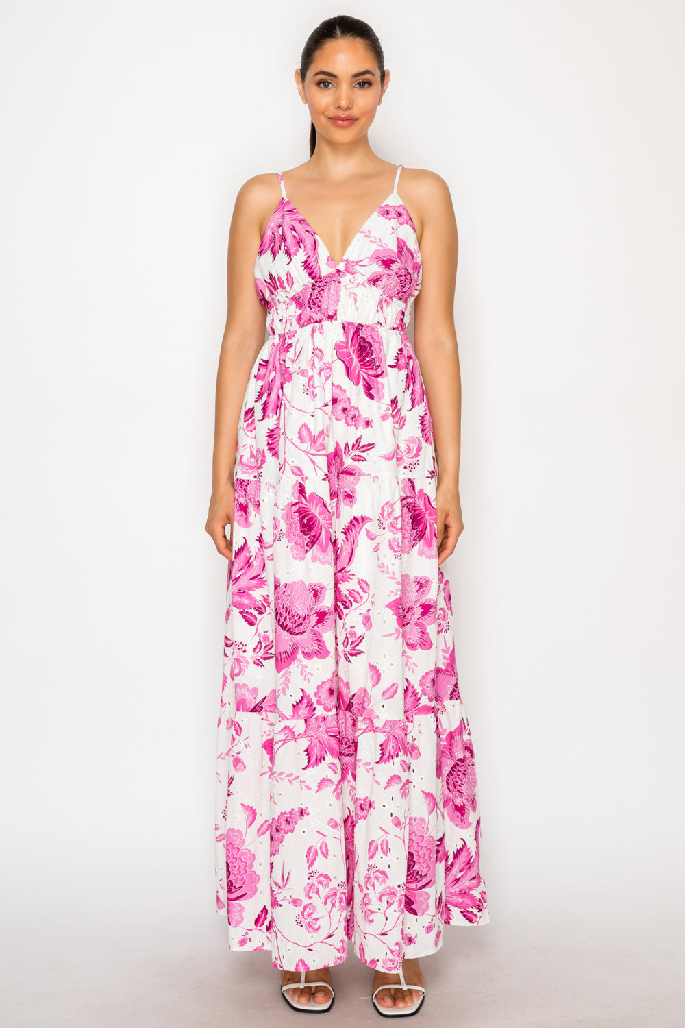 Model wearing the Floral Muse Maxi Dress, a white floor-length tiered dress with a vibrant magenta floral print, a deep V-neckline, and thin straps.