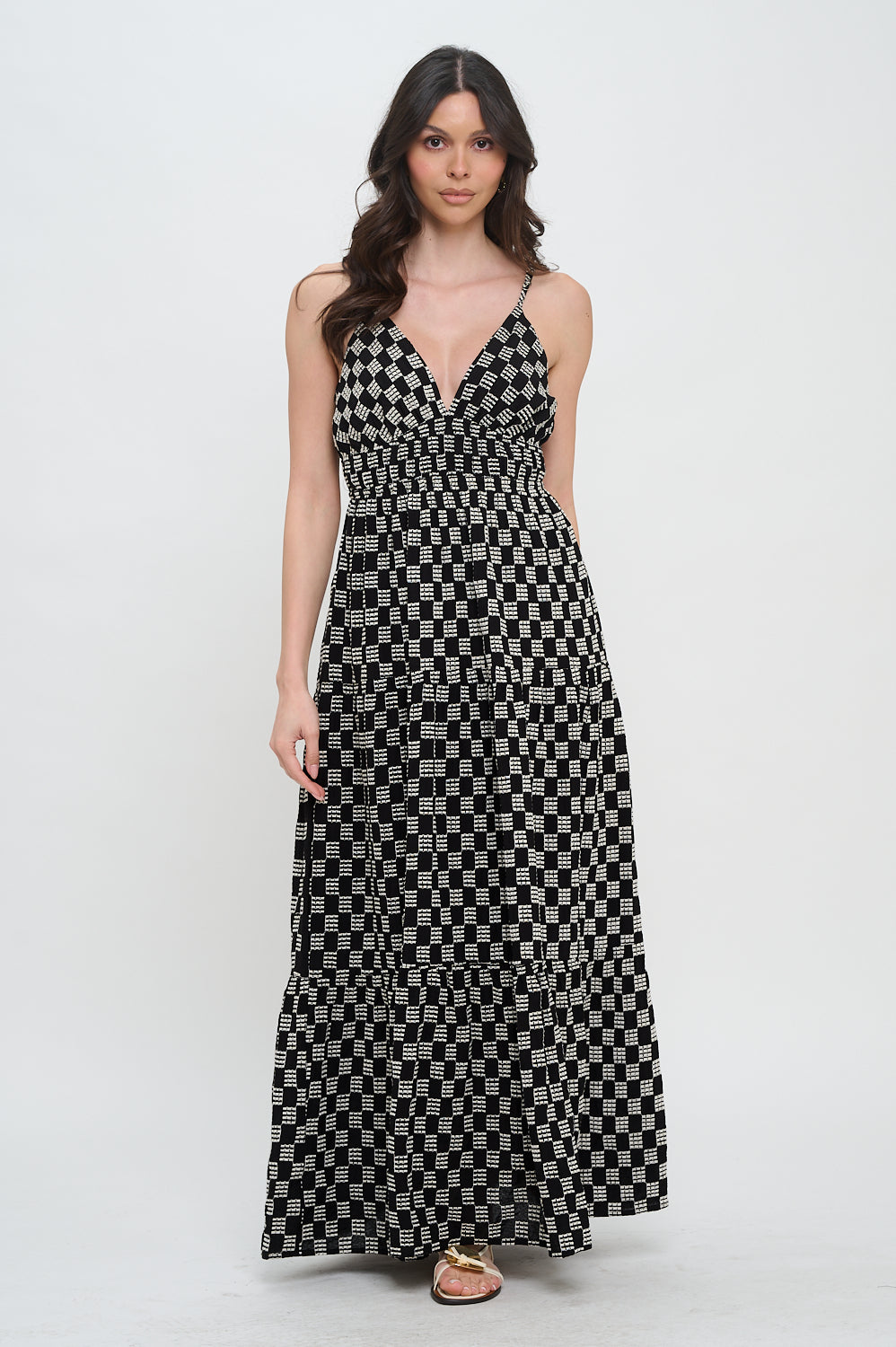 Model wearing the Midnight Weave Maxi Dress from Meet Me in Santorini, a black and white checkerboard print maxi dress with a V-neck and spaghetti straps.