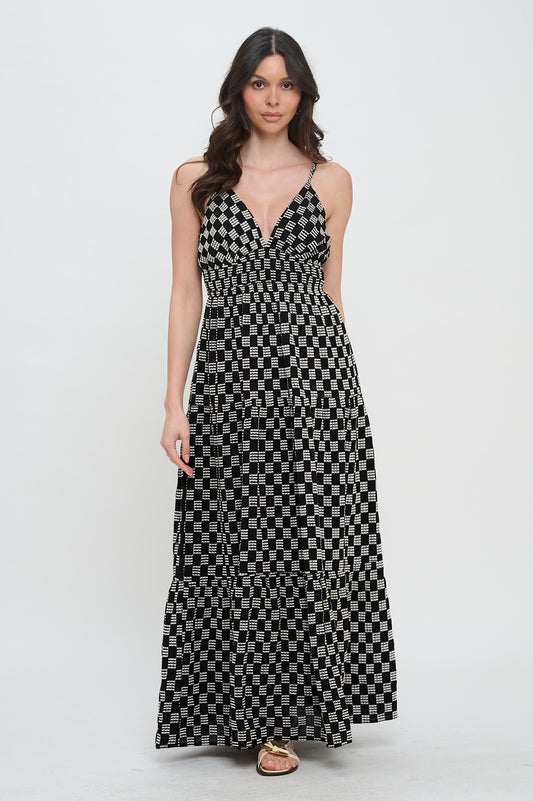 Model wearing the Midnight Weave Maxi Dress from Meet Me in Santorini, a black and white checkerboard print maxi dress with a V-neck and spaghetti straps.