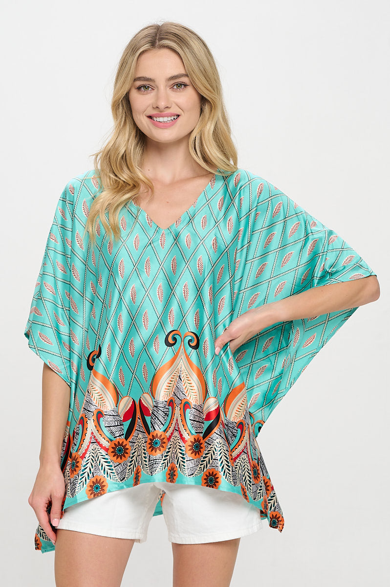 Model wearing a relaxed teal printed top with a V-neckline and border detail, styled with white shorts.