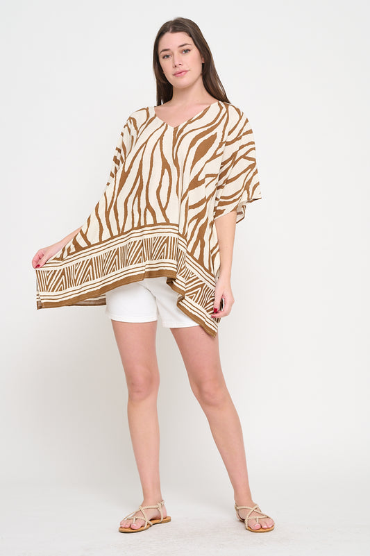Woman wearing a V-neck tunic with zebra-inspired print in earthy tones and geometric border, styled with white shorts.