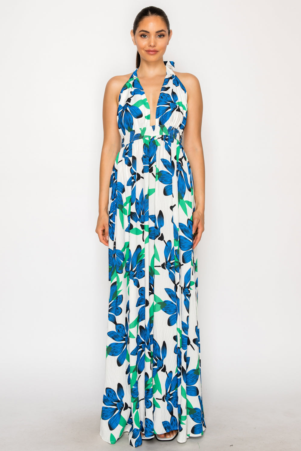 Model wearing the Ocean Lily Maxi Dress, a white floor-length halter dress with a large blue and green floral print and a smocked waist.