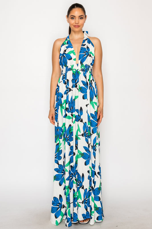 Model wearing the Ocean Lily Maxi Dress, a white floor-length halter dress with a large blue and green floral print and a smocked waist.