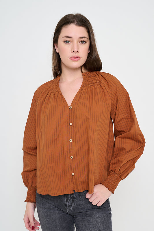 Woman wearing a long sleeve V-neck blouse in terracotta with tonal stripes, button front, and smocked cuffs.