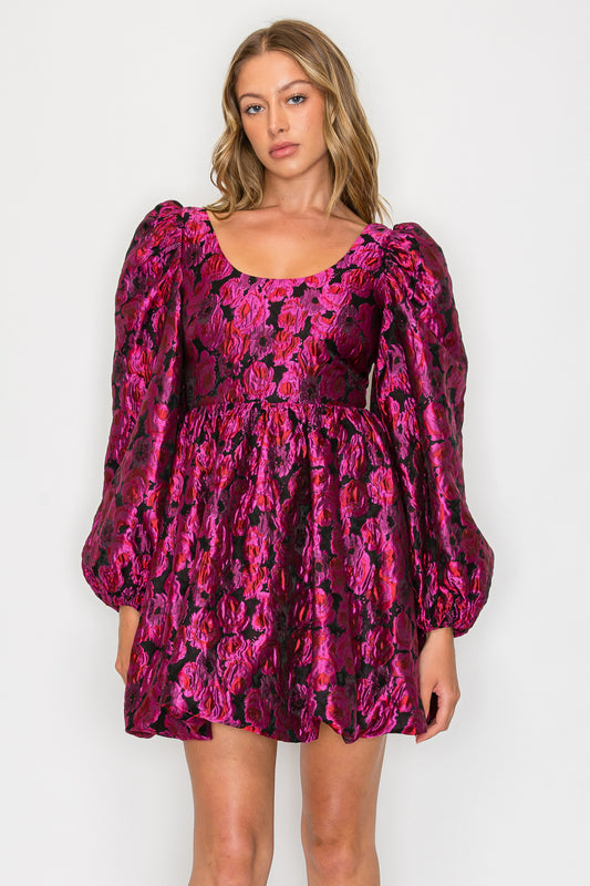 Model wearing the Heras Garland Cecily Dress, a pink and black metallic floral mini dress with a scoop neck and long bishop sleeves.