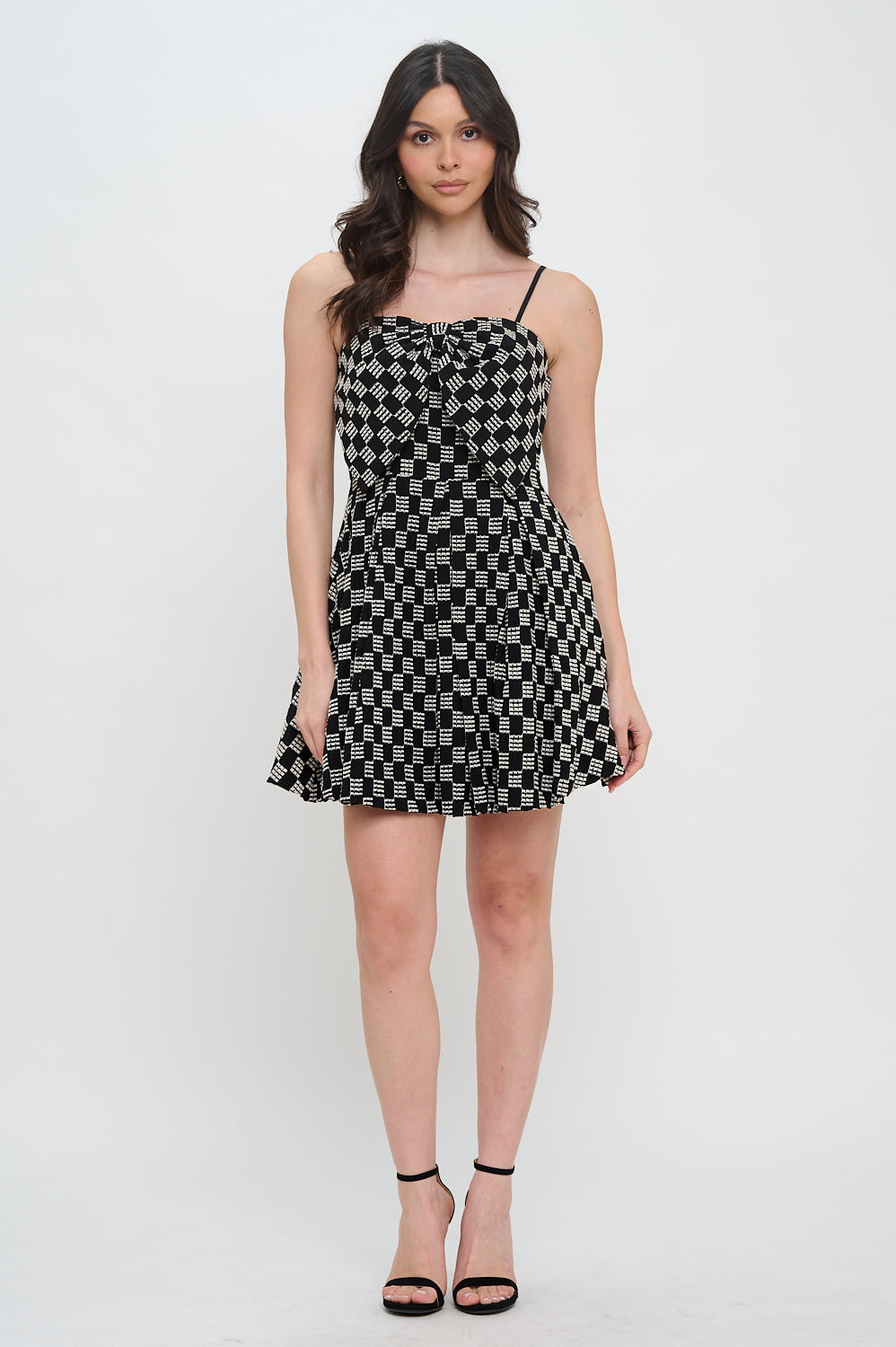 Model wearing the Midnight Weave Bow Mini Dress from Meet Me in Santorini, featuring a black and white checkerboard pattern and a bow detail.
