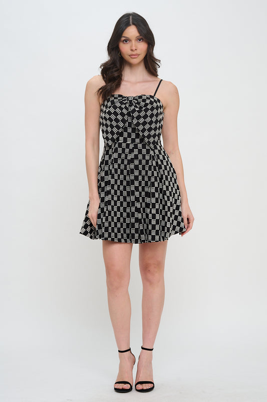 Model wearing the Midnight Weave Bow Mini Dress from Meet Me in Santorini, featuring a black and white checkerboard pattern and a bow detail.