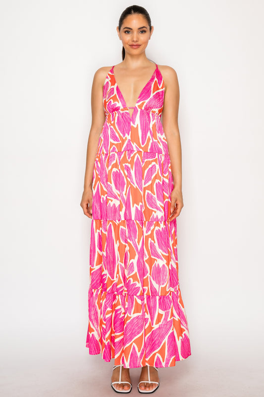 Model wearing Thalia's Tulip Maxi Dress, a white floor-length tiered dress with a vibrant magenta and orange abstract floral print and a deep V-neckline.