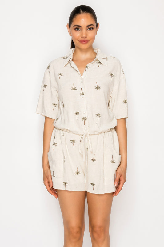 Model wearing the Drifting Palms Set, a cream-colored two-piece set with a palm tree print, featuring a collared top and drawstring shorts.