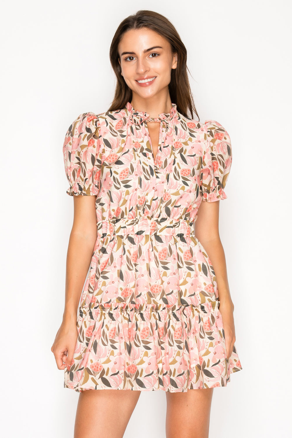 Model wearing the Peony Glow Short Dress, a pink floral mini dress with a ruffle tie-neck, puff sleeves, and a tiered skirt.