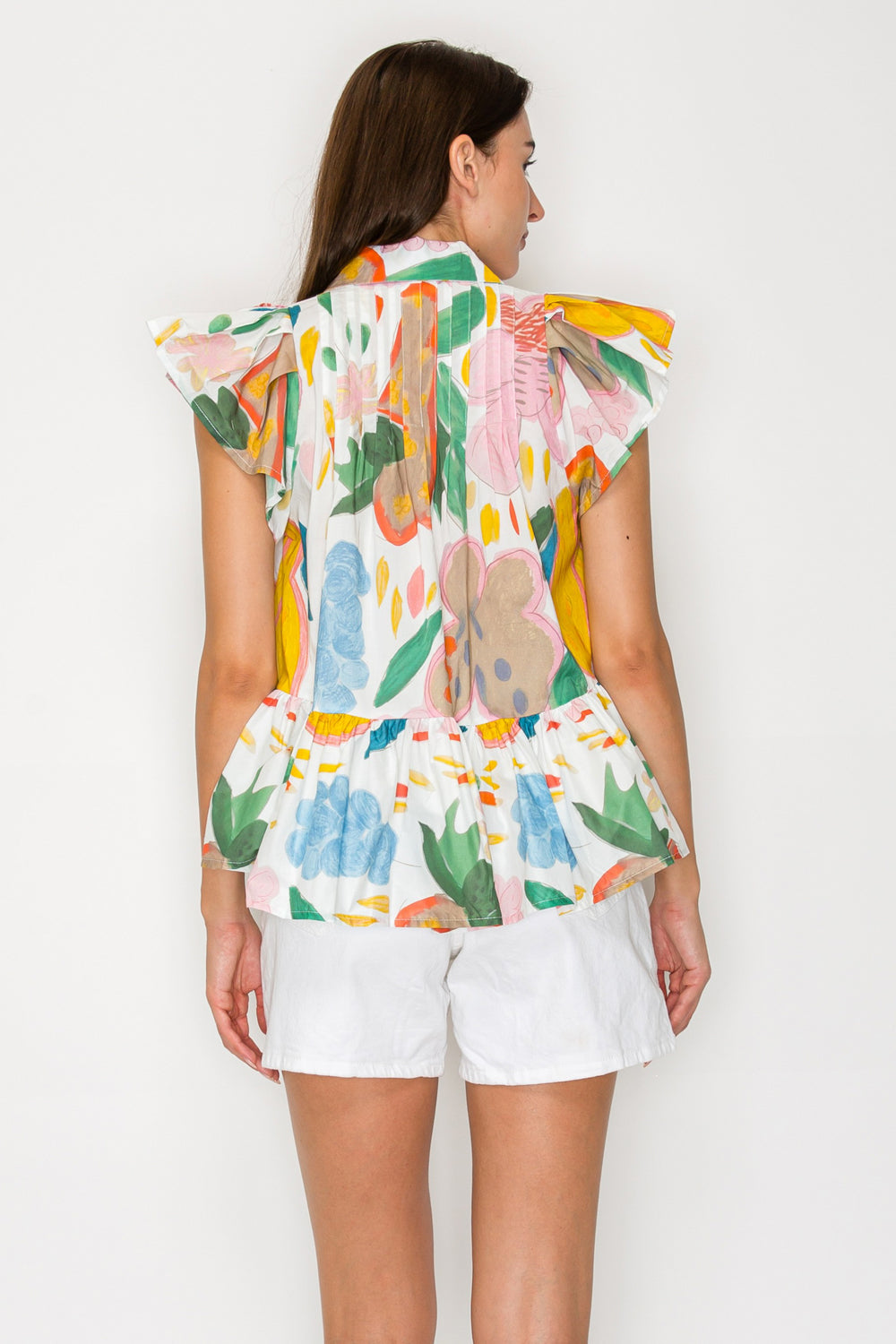 Woman wearing a colorful sleeveless top and white shorts against a plain background