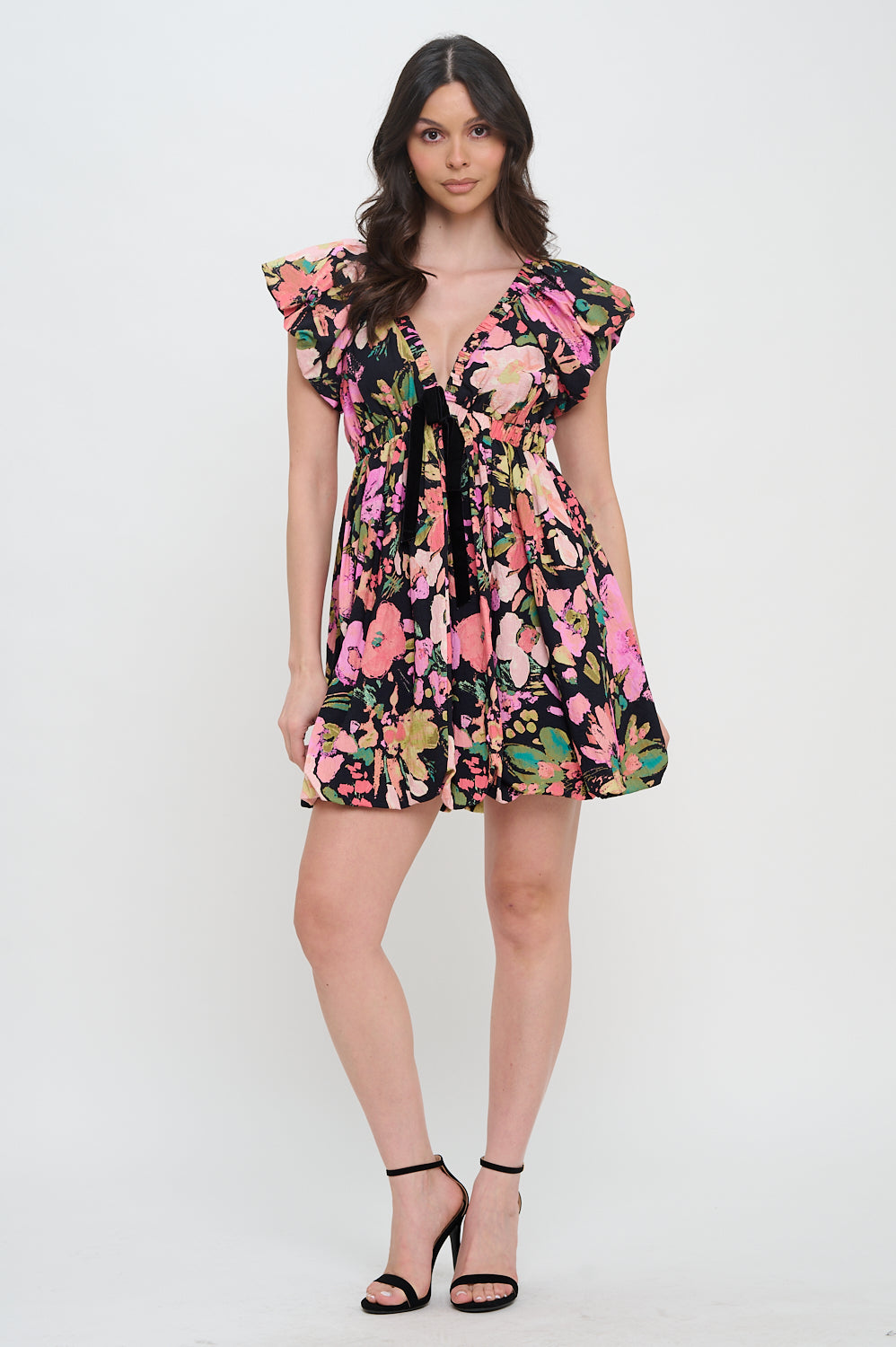 Model wearing the Midnight Garden Bow Trim Dress, a black floral mini dress with a V-neck, flutter sleeves, and a velvet bow at the bust.