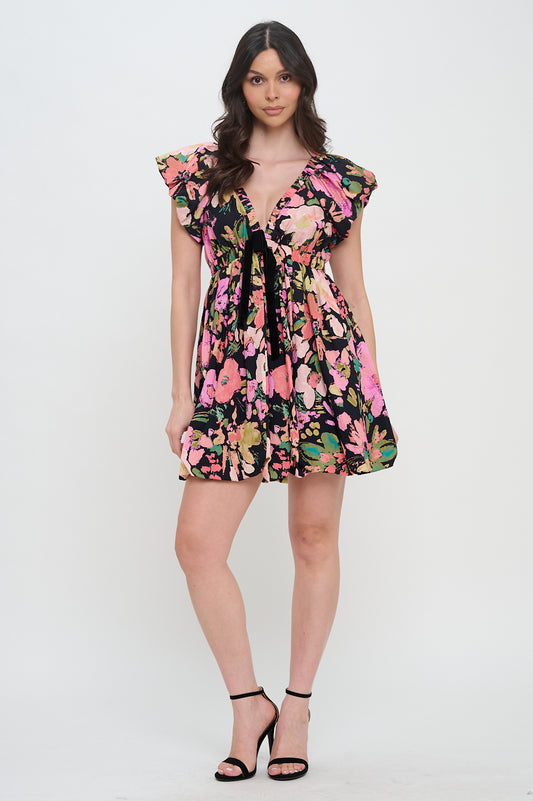 Model wearing the Midnight Garden Bow Trim Dress, a black floral mini dress with a V-neck, flutter sleeves, and a velvet bow at the bust.