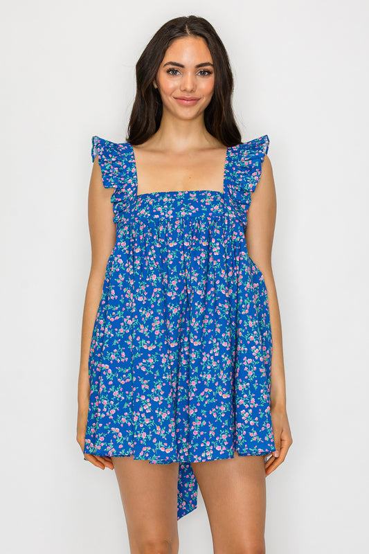 Model wearing a floral babydoll mini dress with ruffle straps, square neckline, and an oversized bow tie-back detail.