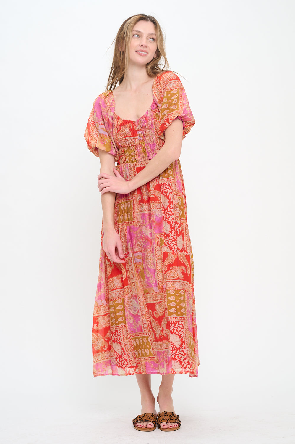 Model wearing the Mediterranean Majesty Maxi Dress, a pink and red paisley print dress with a sweetheart neckline, puff sleeves, and a smocked bodice.

