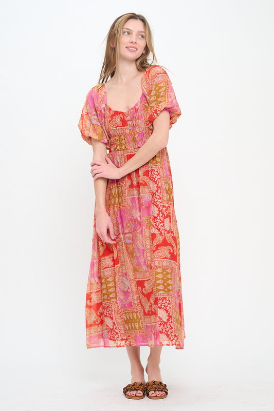 Model wearing the Mediterranean Majesty Maxi Dress, a pink and red paisley print dress with a sweetheart neckline, puff sleeves, and a smocked bodice.

