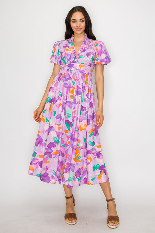 Model wearing a floral maxi dress with flutter sleeves, ruffle neckline, and full skirt in a dreamy lilac multicolor print.