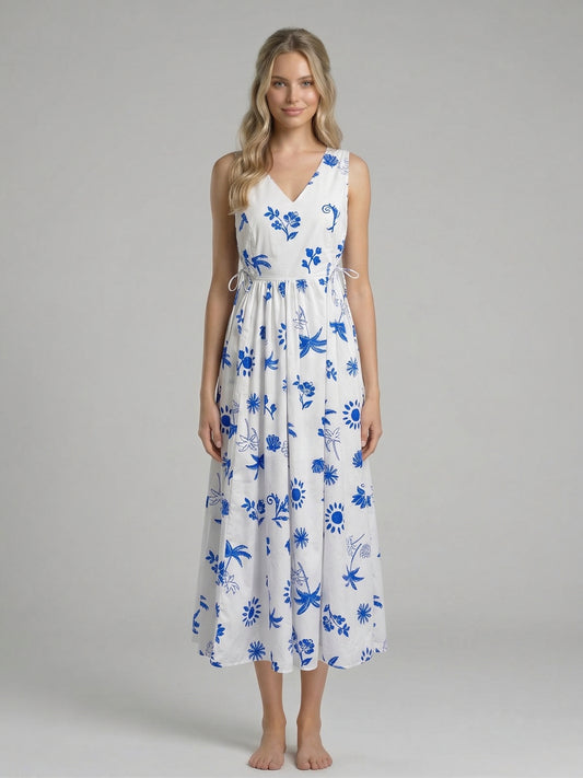 Model wearing the Island Azure Maxi Dress, a white floor-length dress with a vibrant blue tropical and floral print, featuring a V-neckline and side cut-outs with ties.