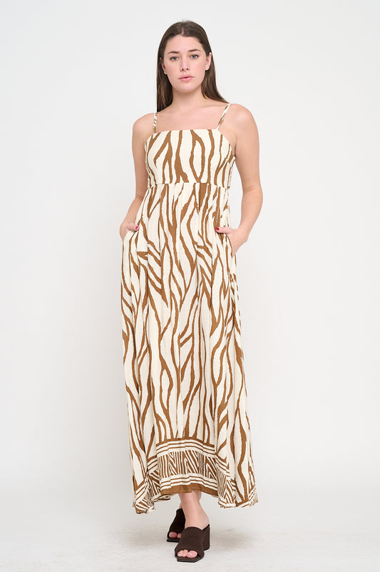 Woman wearing a cotton maxi dress with a square neckline, zebra-inspired print, geometric border hem, adjustable straps, and side pockets.