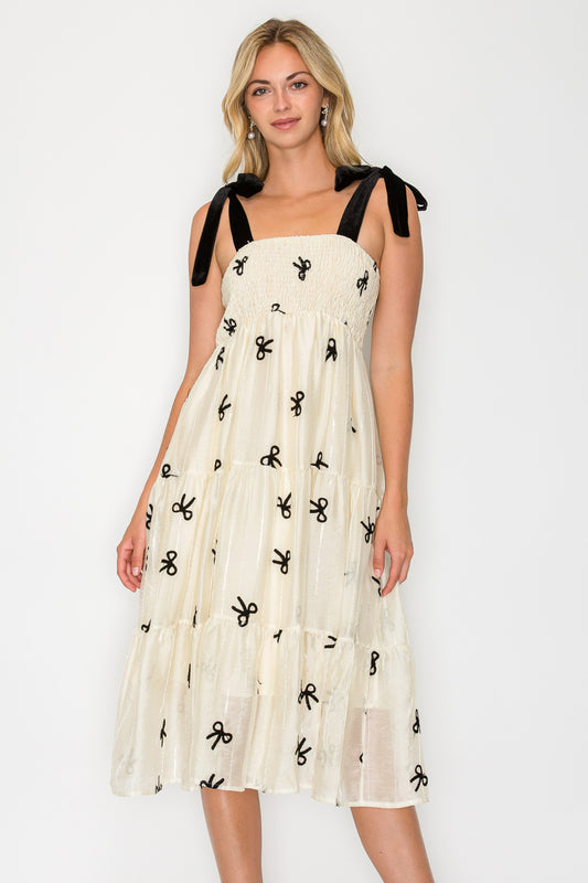 Model wearing the Organza Bow Velvet Tie Midi Dress, a cream-colored dress with a smocked bodice, velvet tie-shoulders, and a tiered midi skirt.