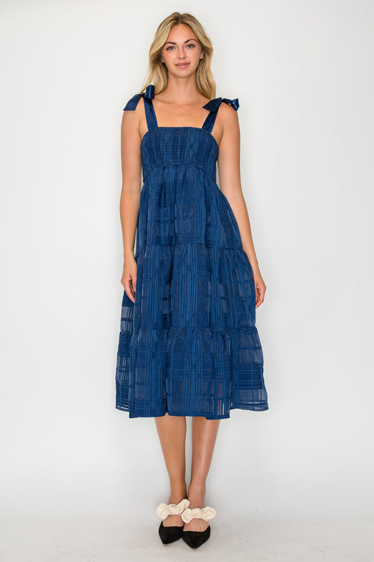 Model wearing the Windowpane Jacquard Tie Dress, a navy blue midi dress with a smocked bodice, satin tie-shoulders, and a tiered skirt.