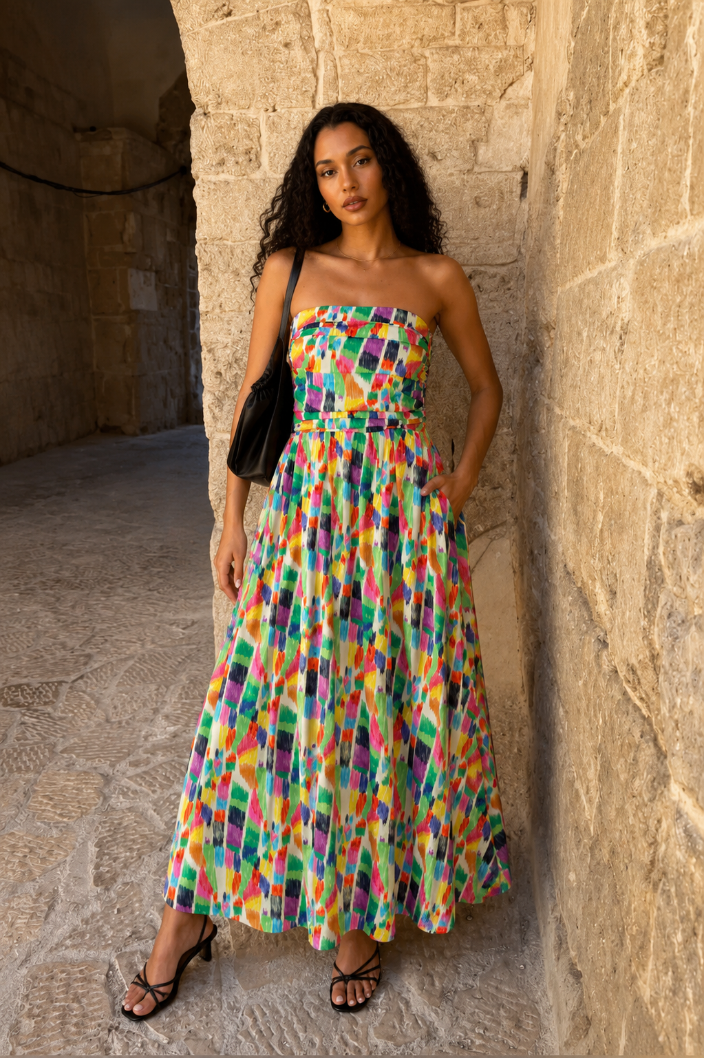 Woman in a colorful strapless dress standing against a stone wall.