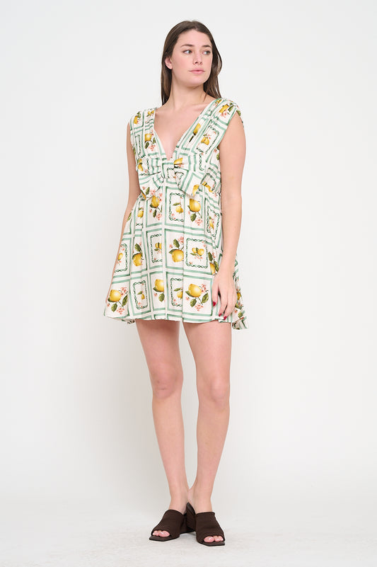 Woman wearing a cotton short dress with plunging neckline, bow detail, and lemon-and-blossom print framed by green stripes.