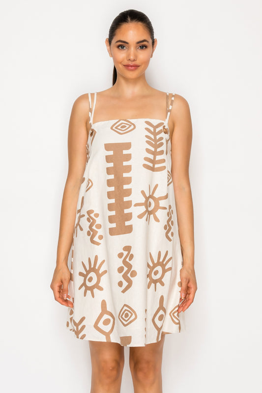 Model wearing the Santorini Sunplay Mini Dress, a cream-colored shift dress with brown abstract symbols and double spaghetti straps.