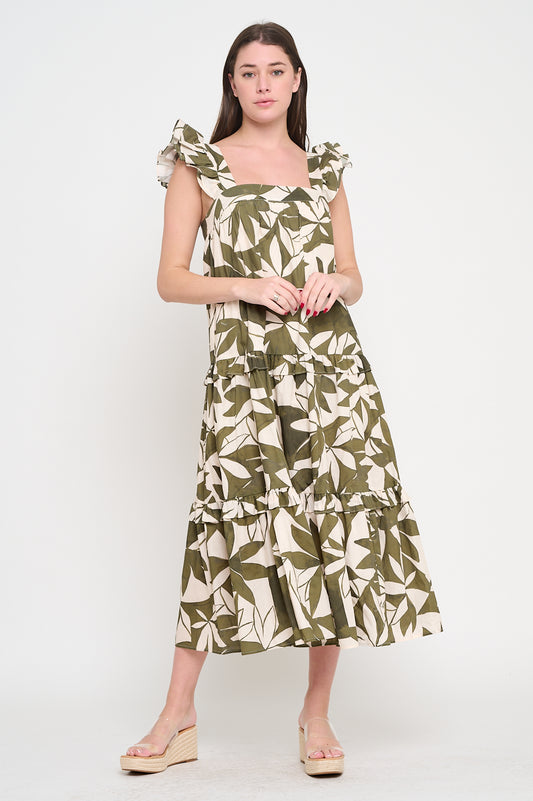 Woman wearing a sleeveless maxi dress with ruffle straps and a green-and-cream leaf print, featuring a tiered A-line silhouette.