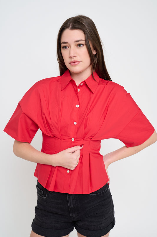Woman wearing a structured button-up poplin shirt with pintuck detail, exaggerated sleeves, and peplum hem.
